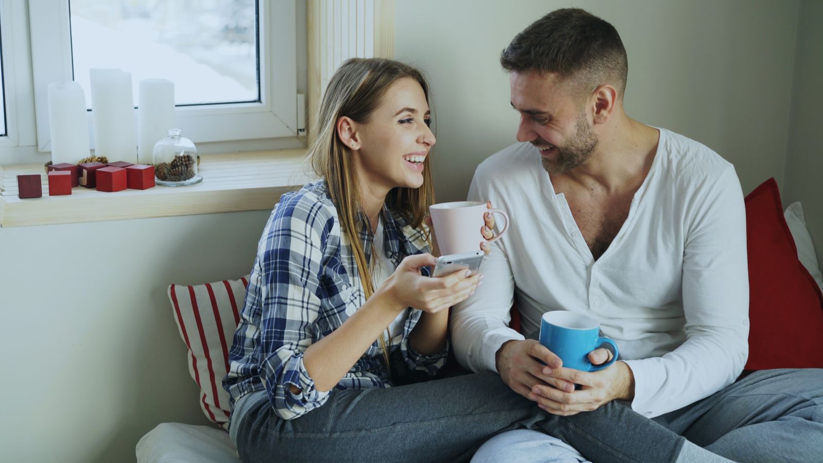Smiling man and woman sharing coffee together on a bright couch, relaxed and supportive